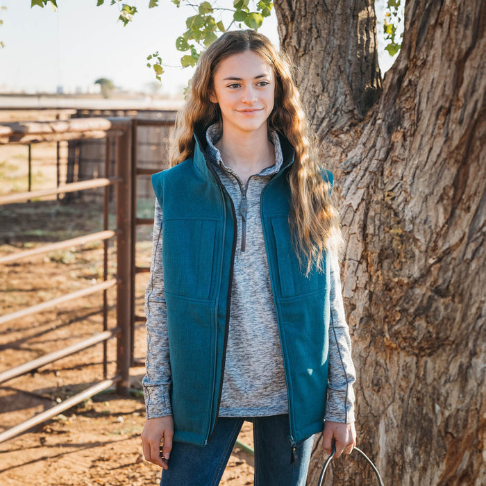 Woman wearing a heather gray long sleeve pullover and teal vest standing in front of a tree.