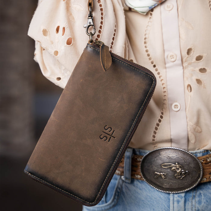 Person holding brown genuine leather wallet with STS stamped into the middle of the wallet.