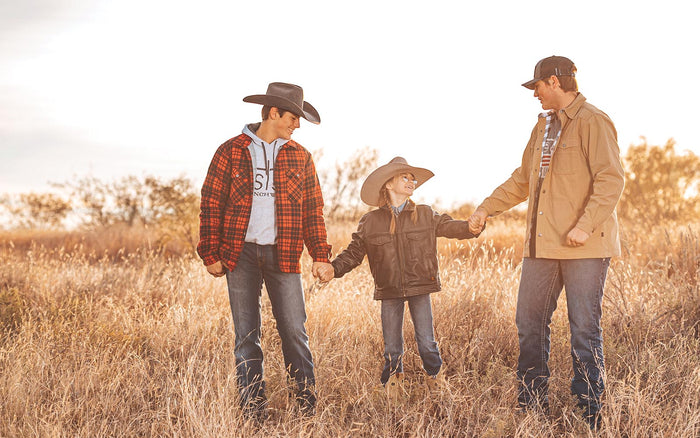 Two brothers hold their sisters hand while standing in a field.