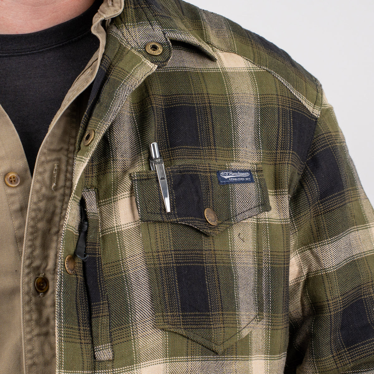 Person wearing a long-sleeved plaid men's shirt jacket with snap closure chest pocket and pen holder on a gray background.