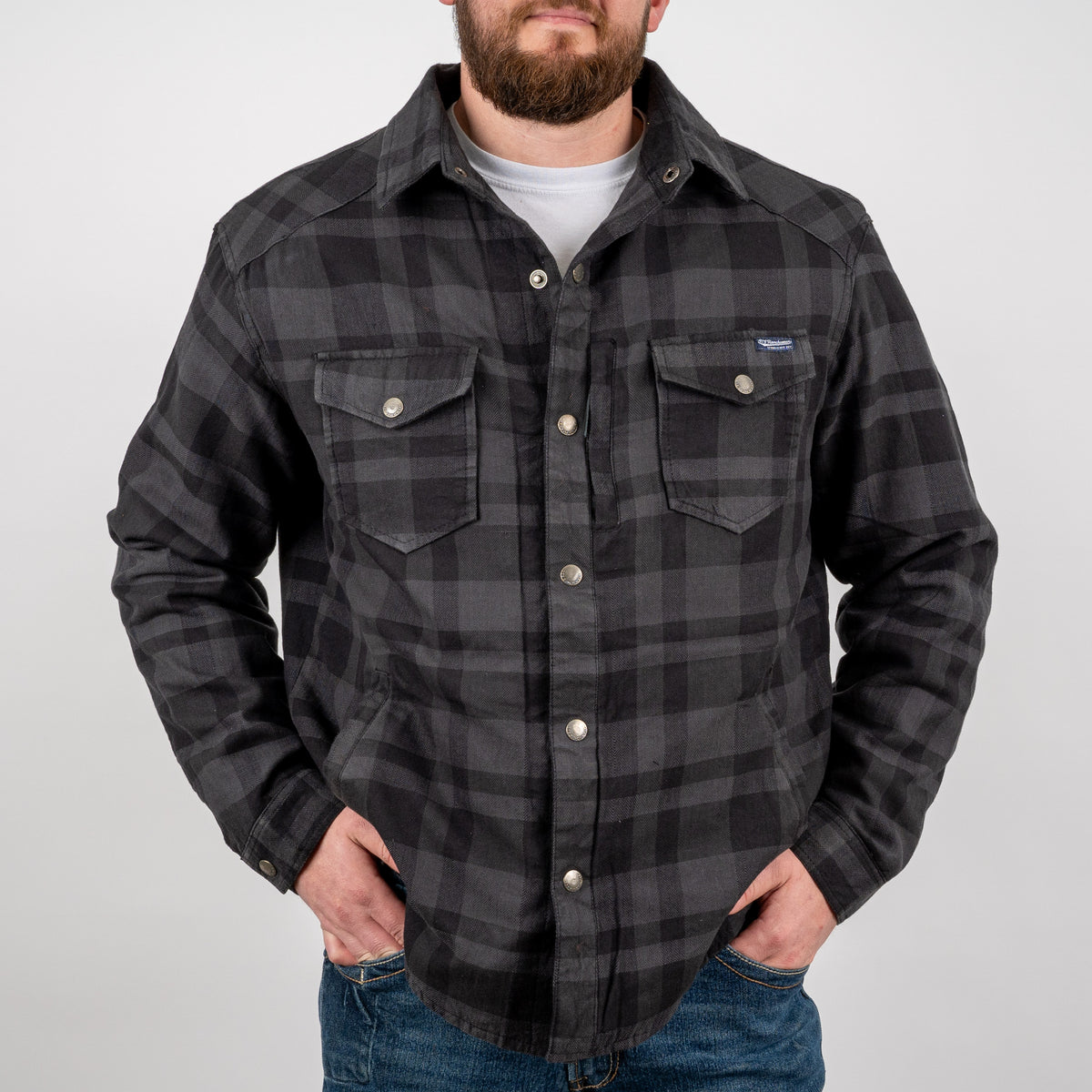 Man wearing a long-sleeved black plaid men's shirt jacket with hand warming pockets and snap closures on a gray background.