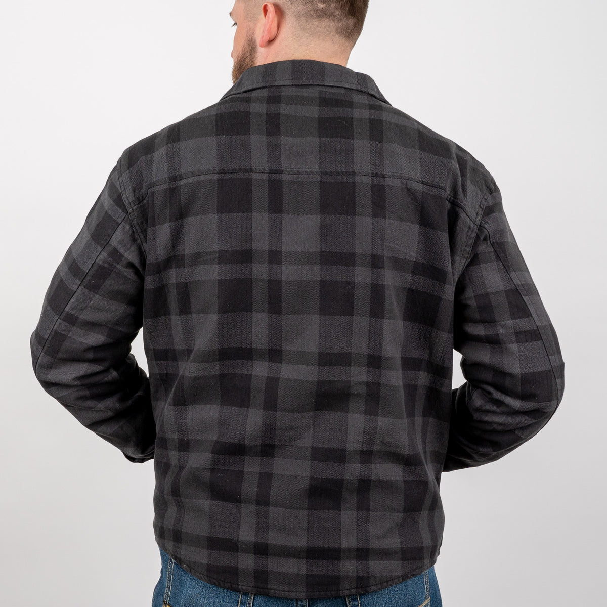 Man facing away wearing a long-sleeved black plaid men's shirt jacket on a gray background.