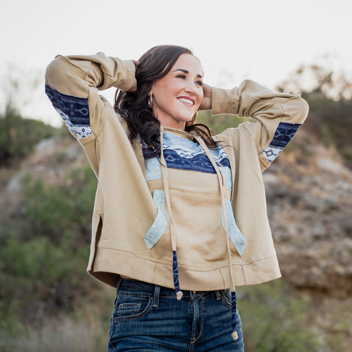 Woman wearing a beige jacket with blue patterns on the chest and sleeves outdoors.