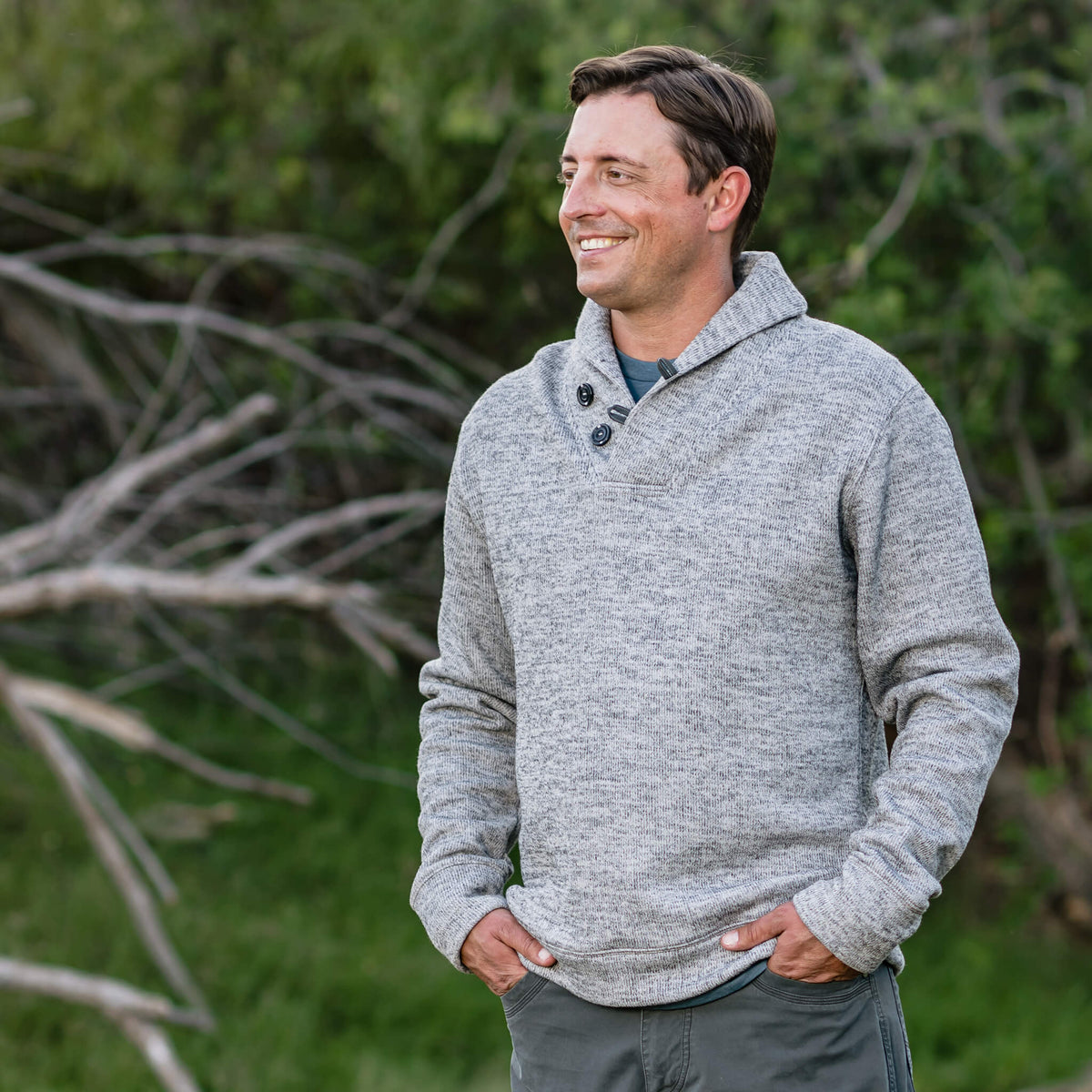 Man in an outdoor setting wearing a gray Olathe pullover with button cowl neck and fleece lining, featuring ribbed cuffs and waistband.