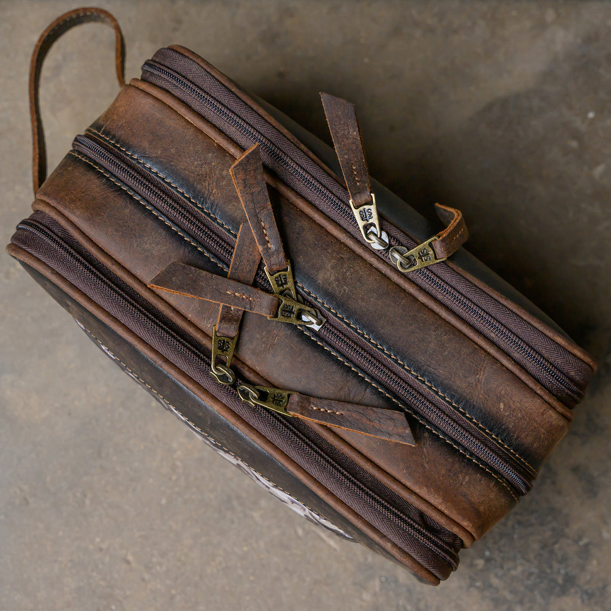 closeup of the top view of our canvas bull camo and full grain leather triple zip closure shave kit on cement ground
