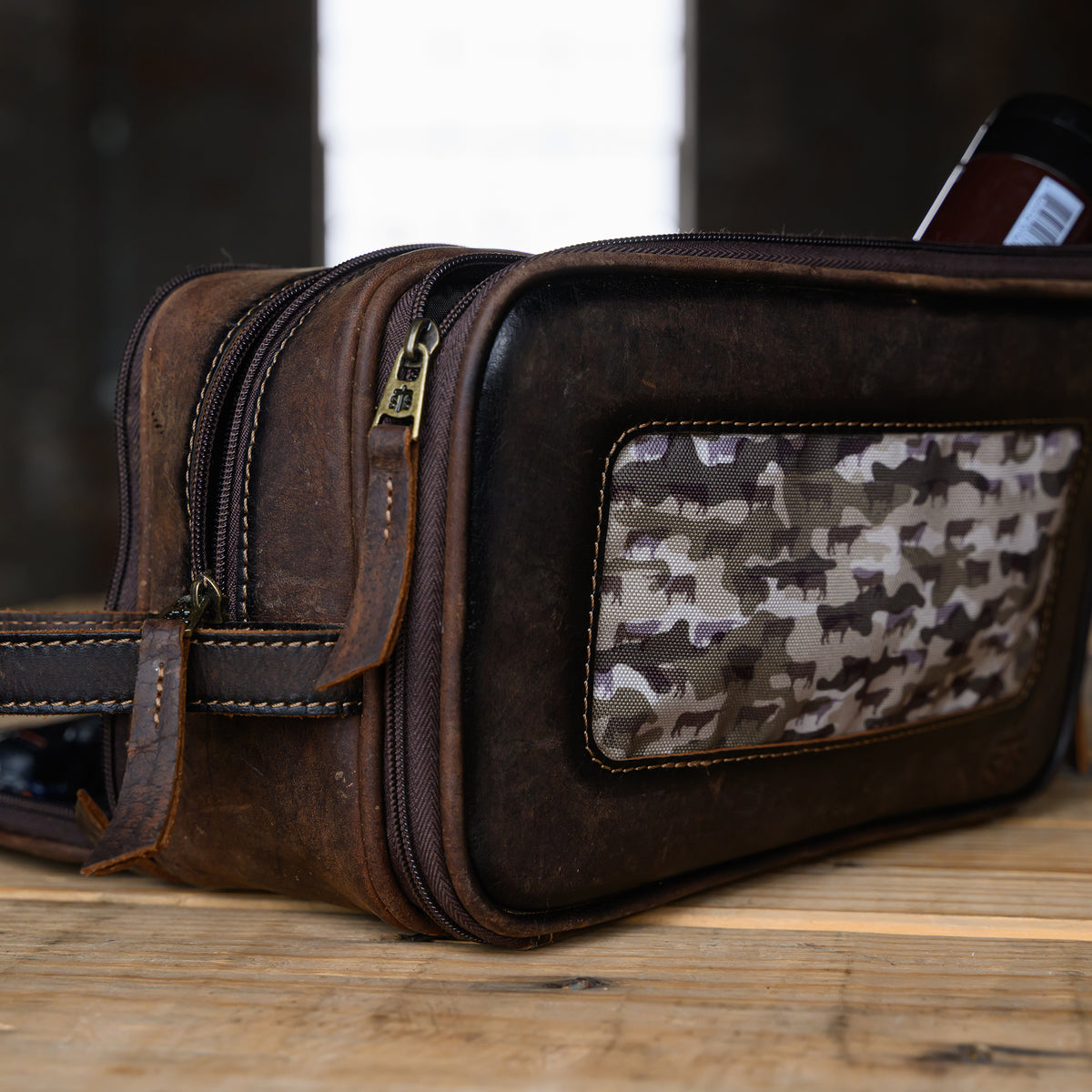 front side view of our canvas bull camo and full grain leather triple zip closure shave kit on wooden table