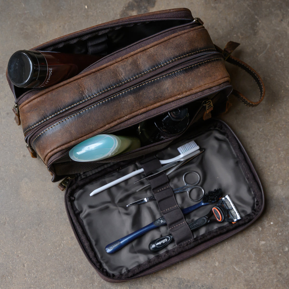 side open view of toiletries in our canvas bull camo and full grain leather triple zip closure shave kit on cement ground