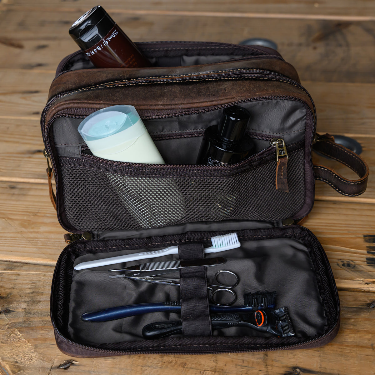 open view of toiletries in our canvas bull camo and full grain leather triple zip closure shave kit on wooden table