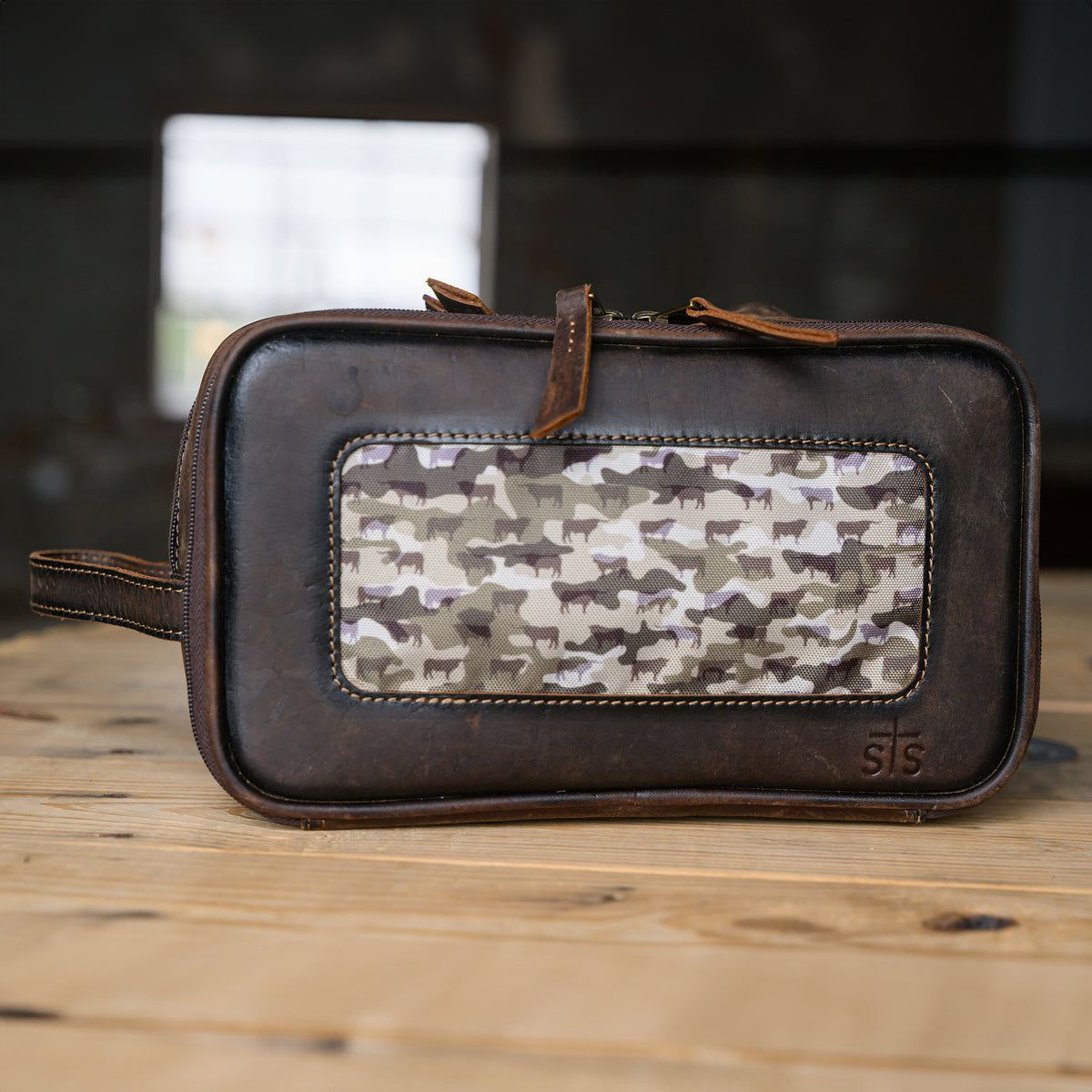 closeup of our canvas bull camo and full grain leather triple zip closure shave kit on wooden table