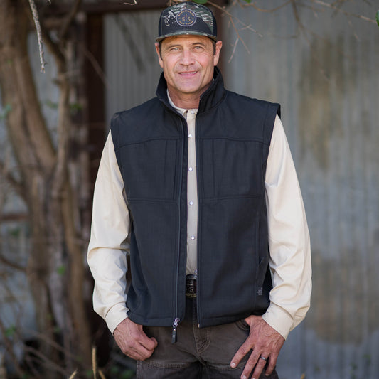 Stran Smith wearing a black vest over a cream long sleeve shirt.