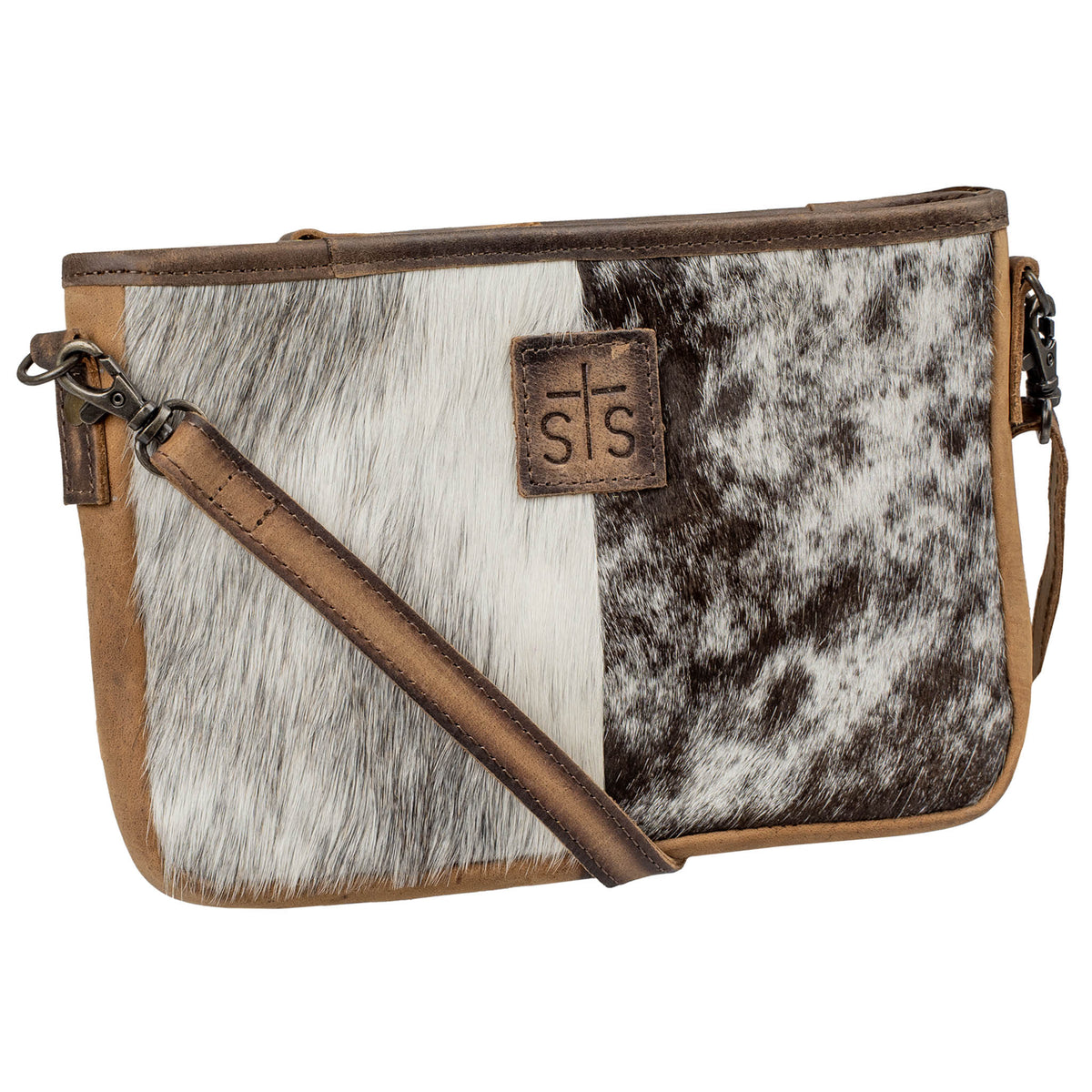A hair on hide cowhide crossbody bag with cowhide pattern and brown leather accents and a brown leather crossbody strap on a white background.