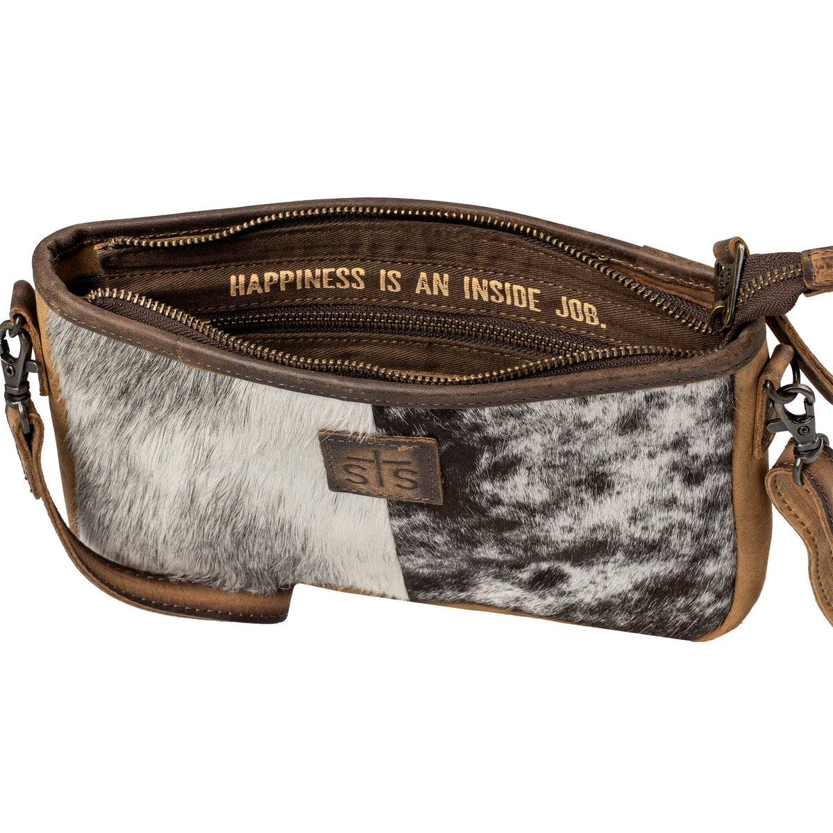 Inside of a hair on hide cowhide crossbody bag with cowhide pattern and brown leather accents, zip closure and interior motivational quote "Happiness is an inside job." on a white background.