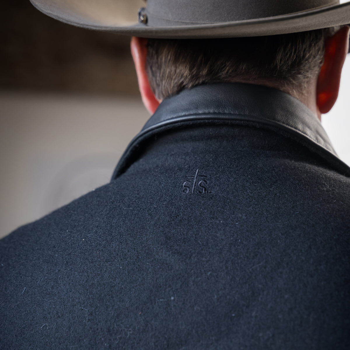 closeup of the back of the collar of our black wool vest with leather collar front zip and snap closure and two waist pockets on white background