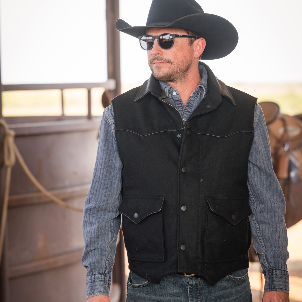 Man wearing sunglasses, a cowboy hat and our black wool vest with leather collar front zip and snap closure and two waist pockets in front of a brown horse