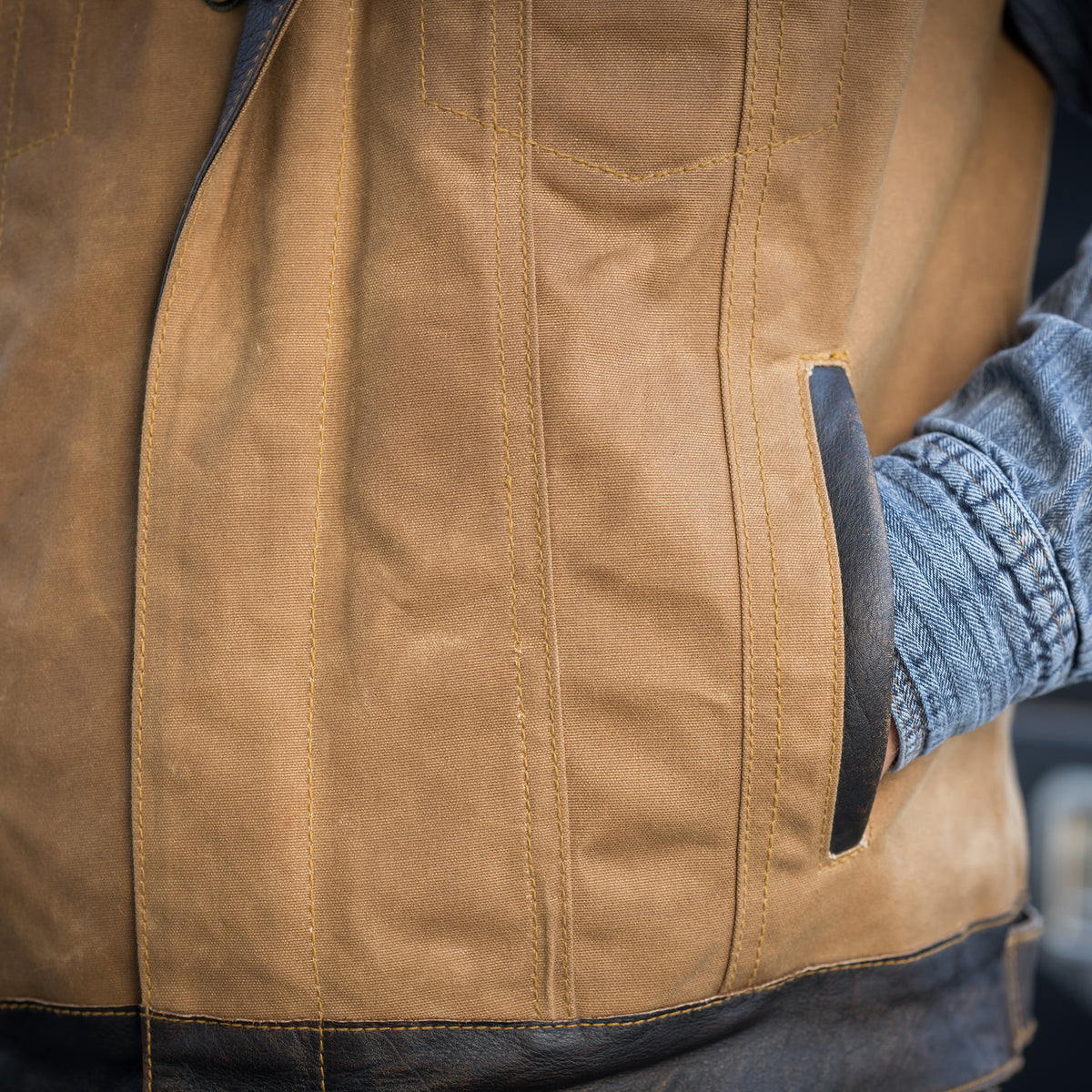 closeup of a hand in the pocket of our snap and zip closure cotton canvas vest with full grain leather accents 