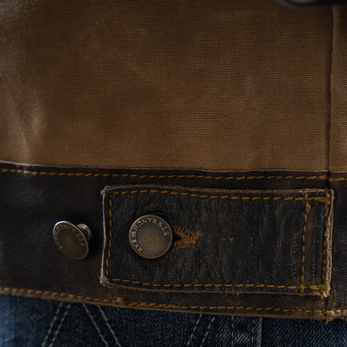 closeup of the bottom button on our snap and zip closure cotton canvas vest with full grain leather accents
