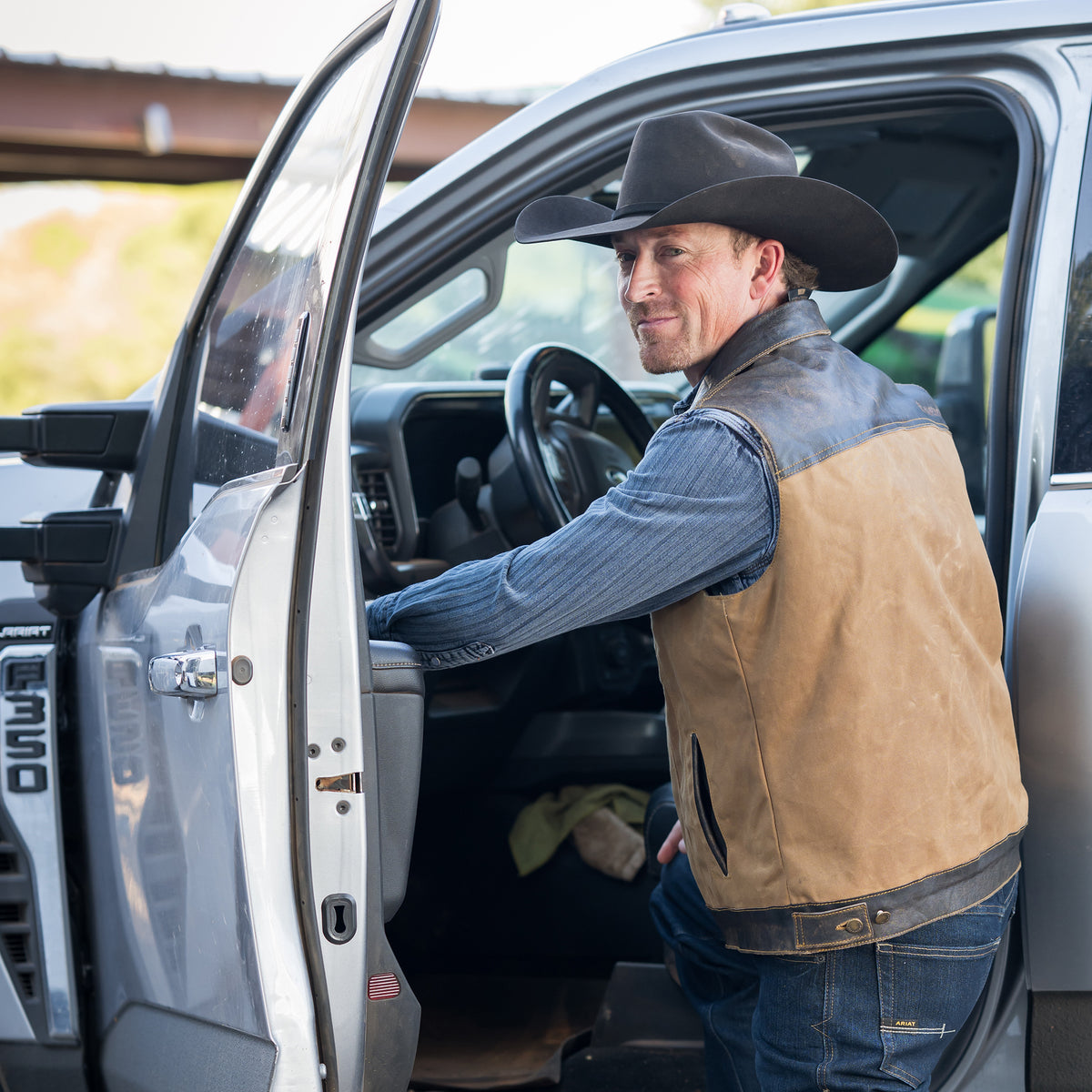 Sawyer Vest entering a truck wearing our snap and zip closure cotton canvas vest with full grain leather accents