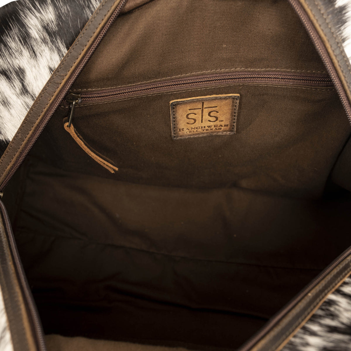 Inside main compartment with zip closure pocket and brown leather patch with STS Ranchwear logo embossed.