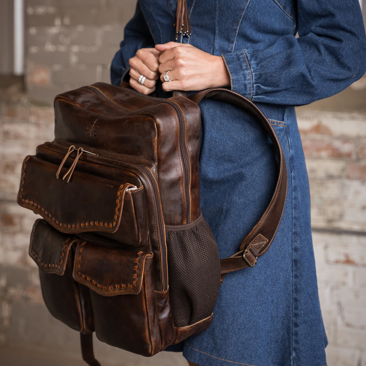 closeup of chenae vest holding our Bandera chocolate leather backpack  with buckstitch, three front magnetic closure pockets and top carry handle 