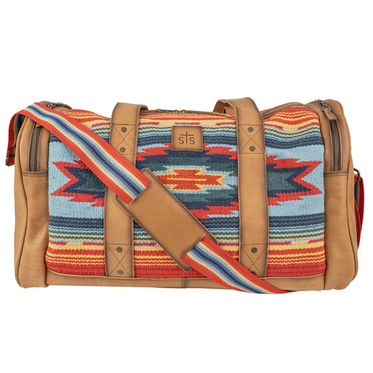 A duffle bag with a vibrant geometric pattern in red, blue, and tan colors, featuring handwoven 100% cotton shell with genuine leather accents, and a shoulder strap.