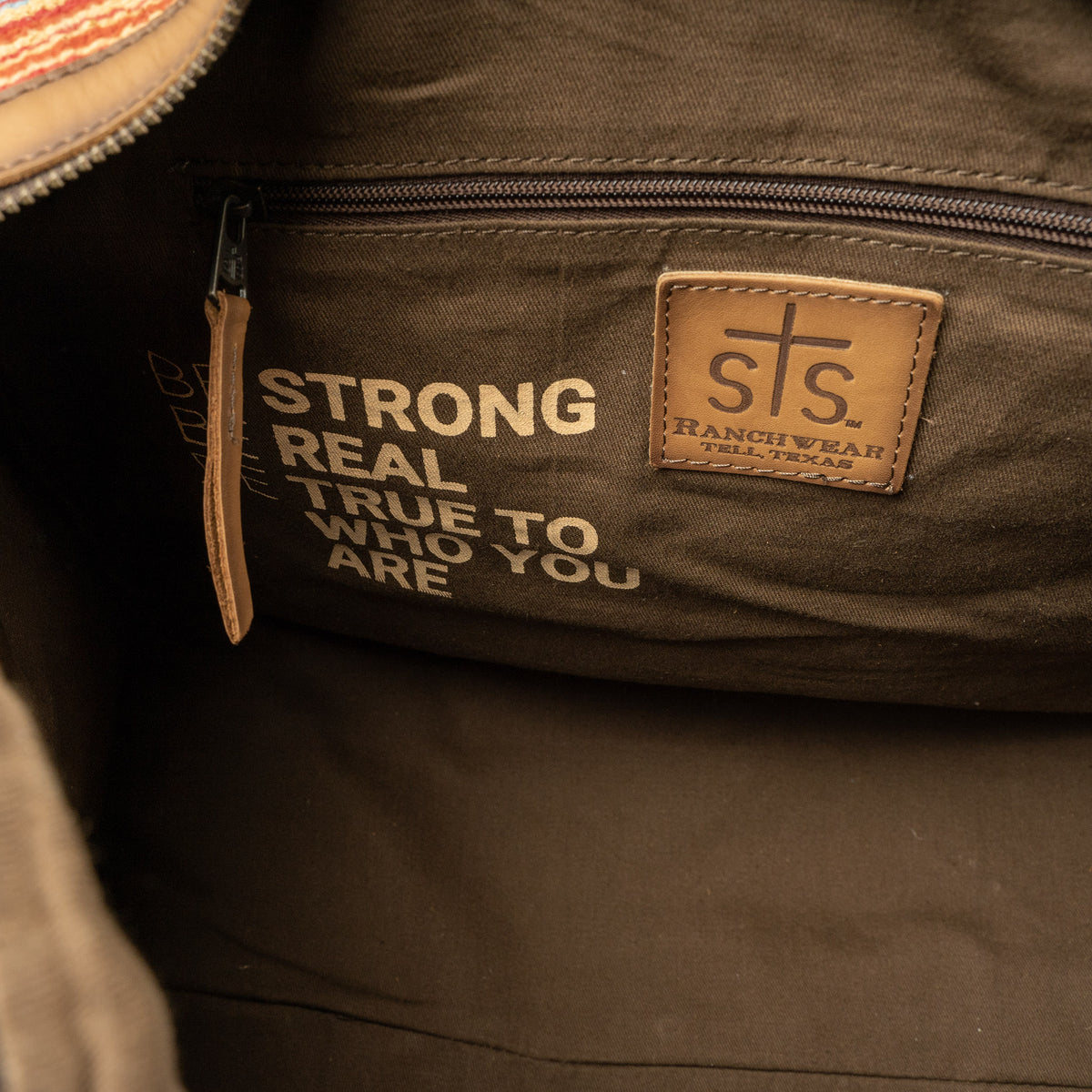 Interior of a duffle bag with brown lining and zip closure pocket.