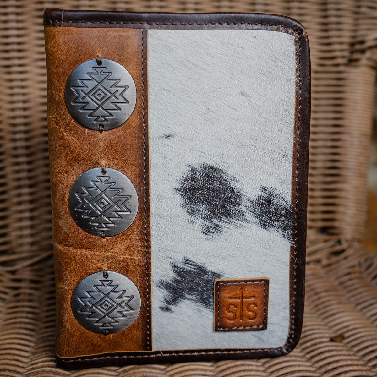 A cowhide magnetic bifold wallet with brown leather edging and three large metal conchos featuring geometric patterns on the front.