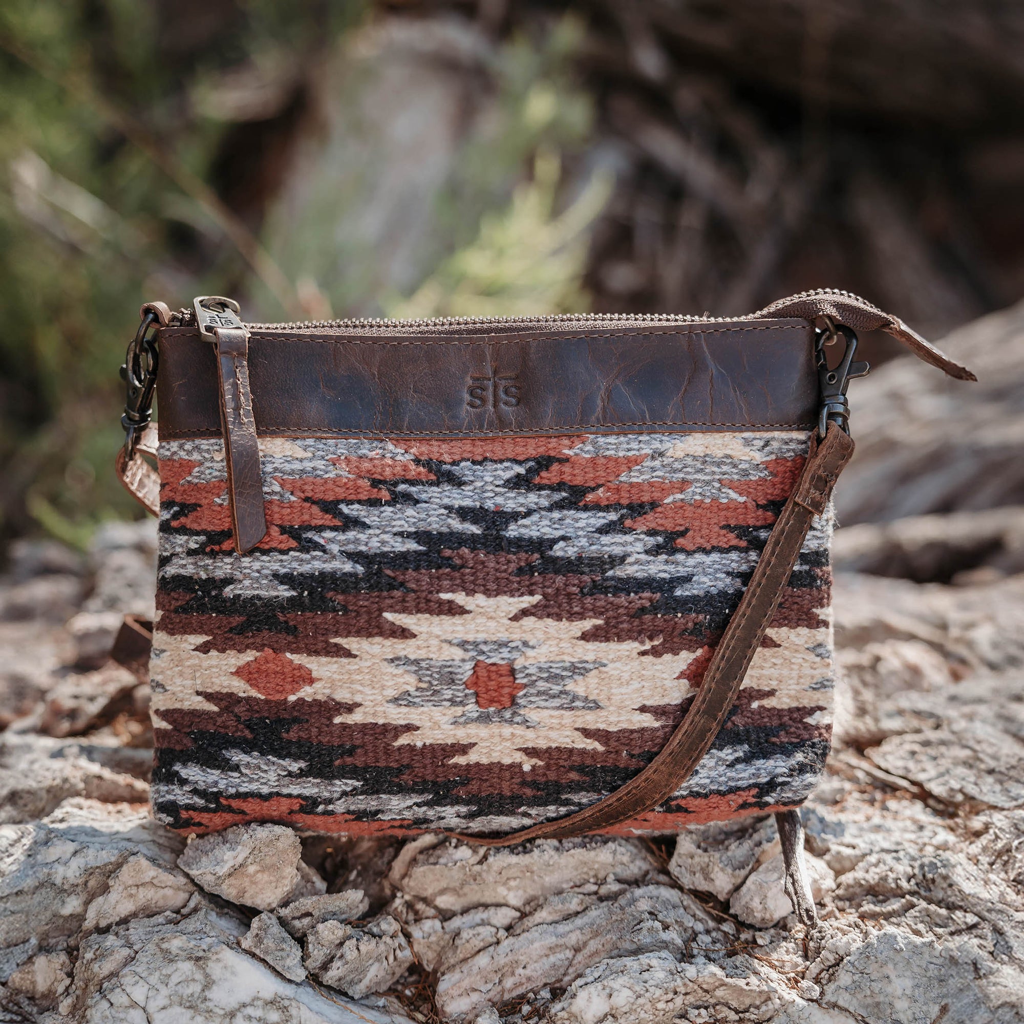 Patterned pouch with leather strap on a rocky surface