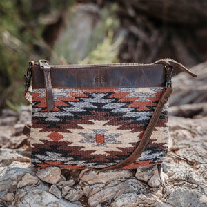 Patterned pouch with leather strap on a rocky surface