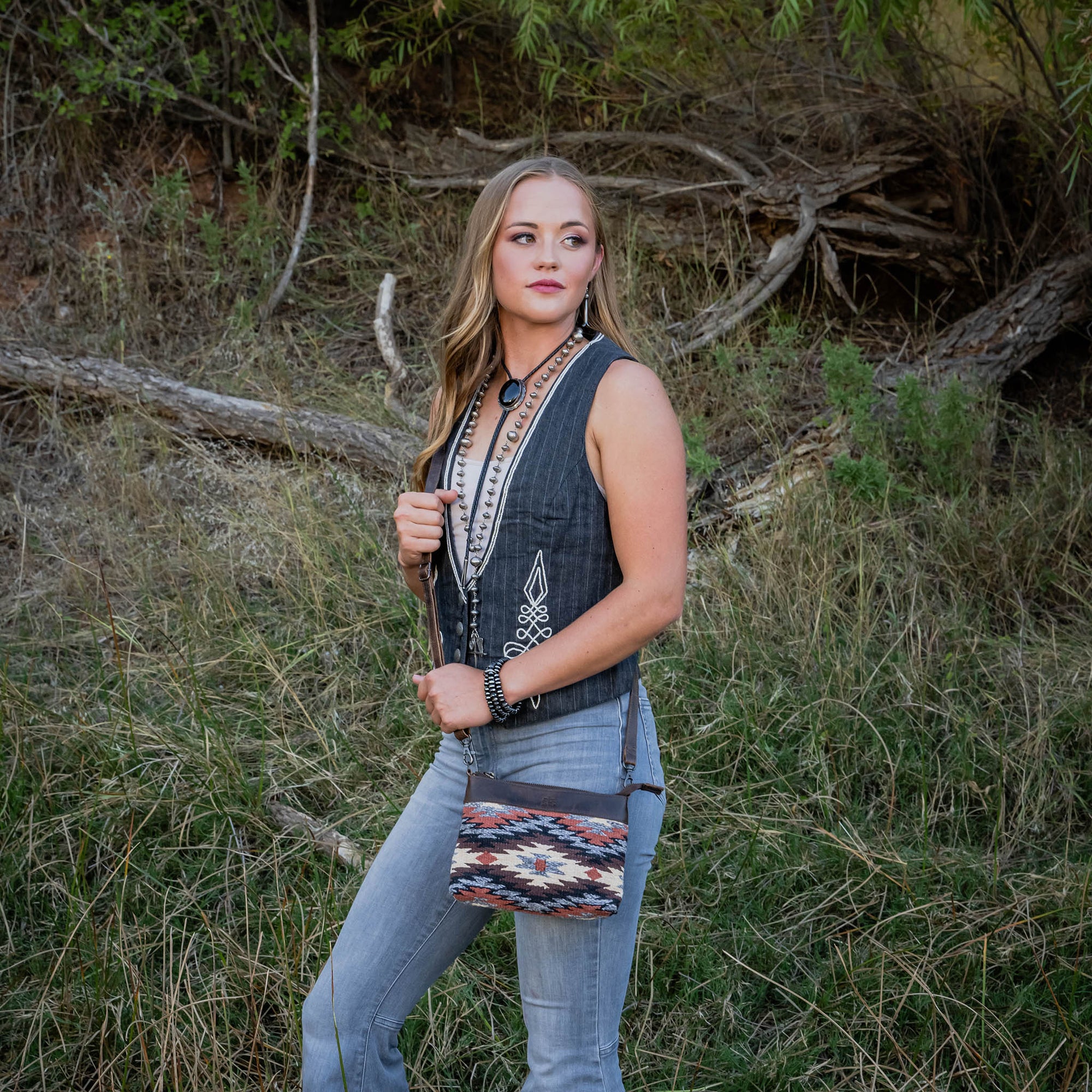 Woman holding a patterned crossbody bag in a natural setting