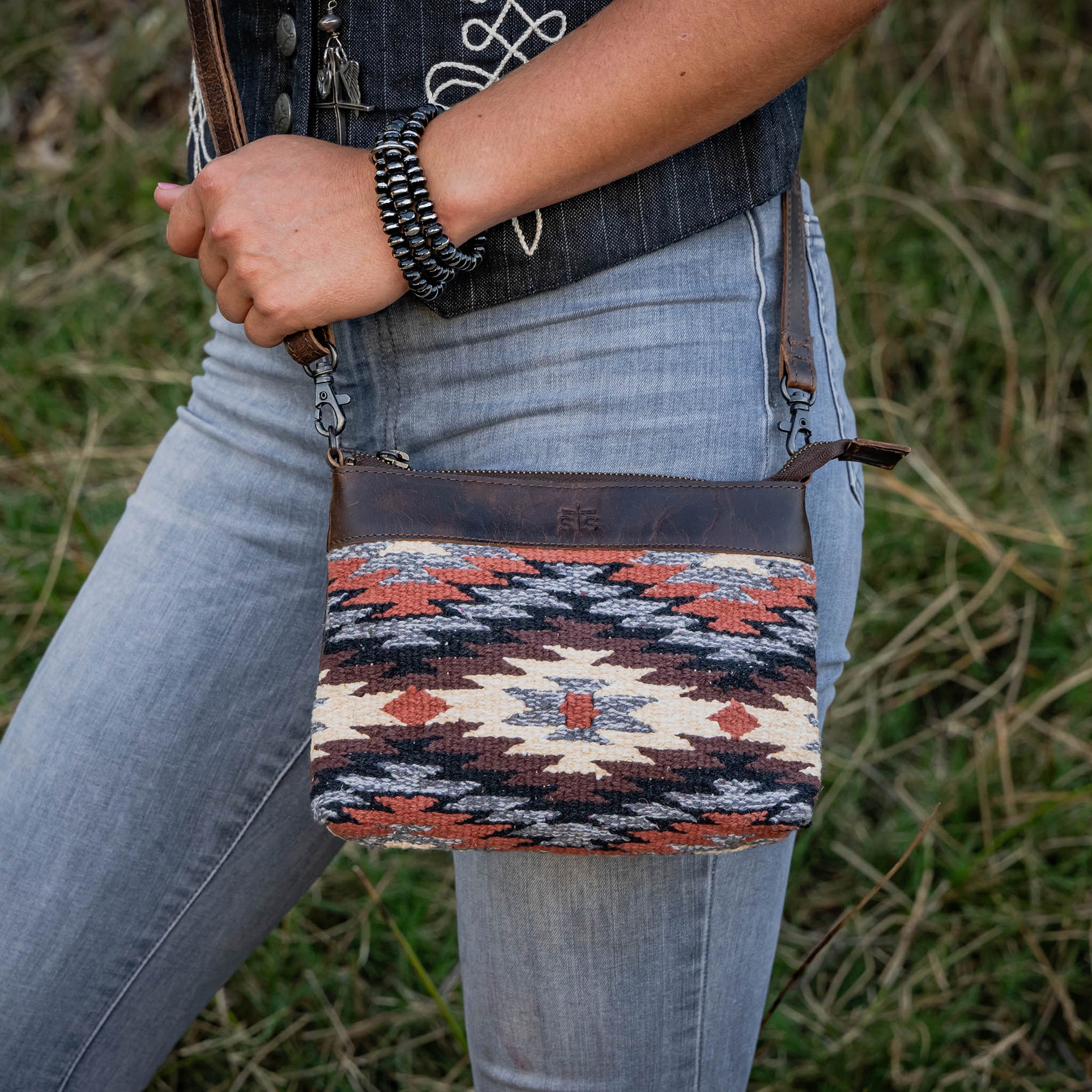 Person holding a patterned clutch bag with a grassy background