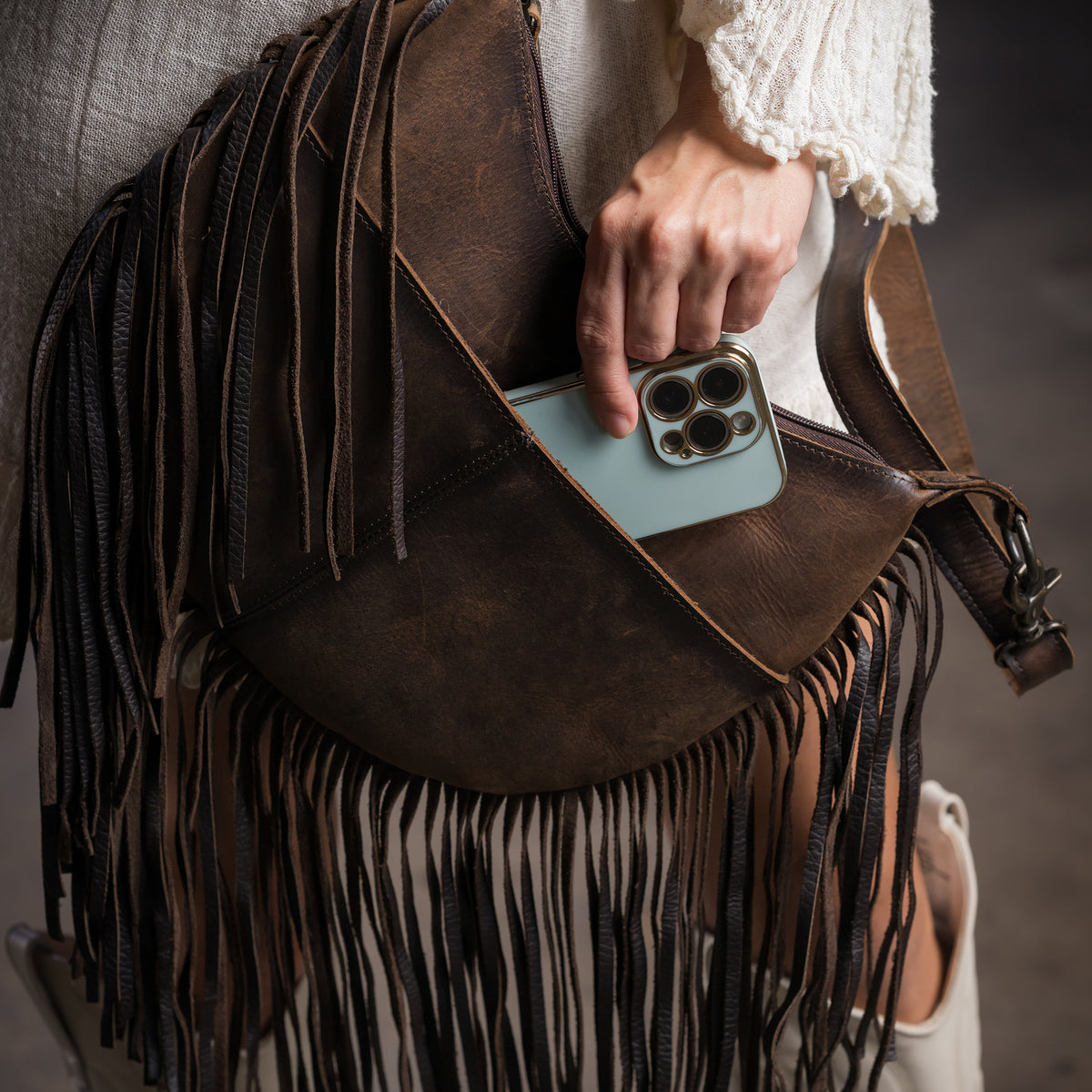 phone being put in the side pocket of our  leather crescent bag with fringe along the bottom