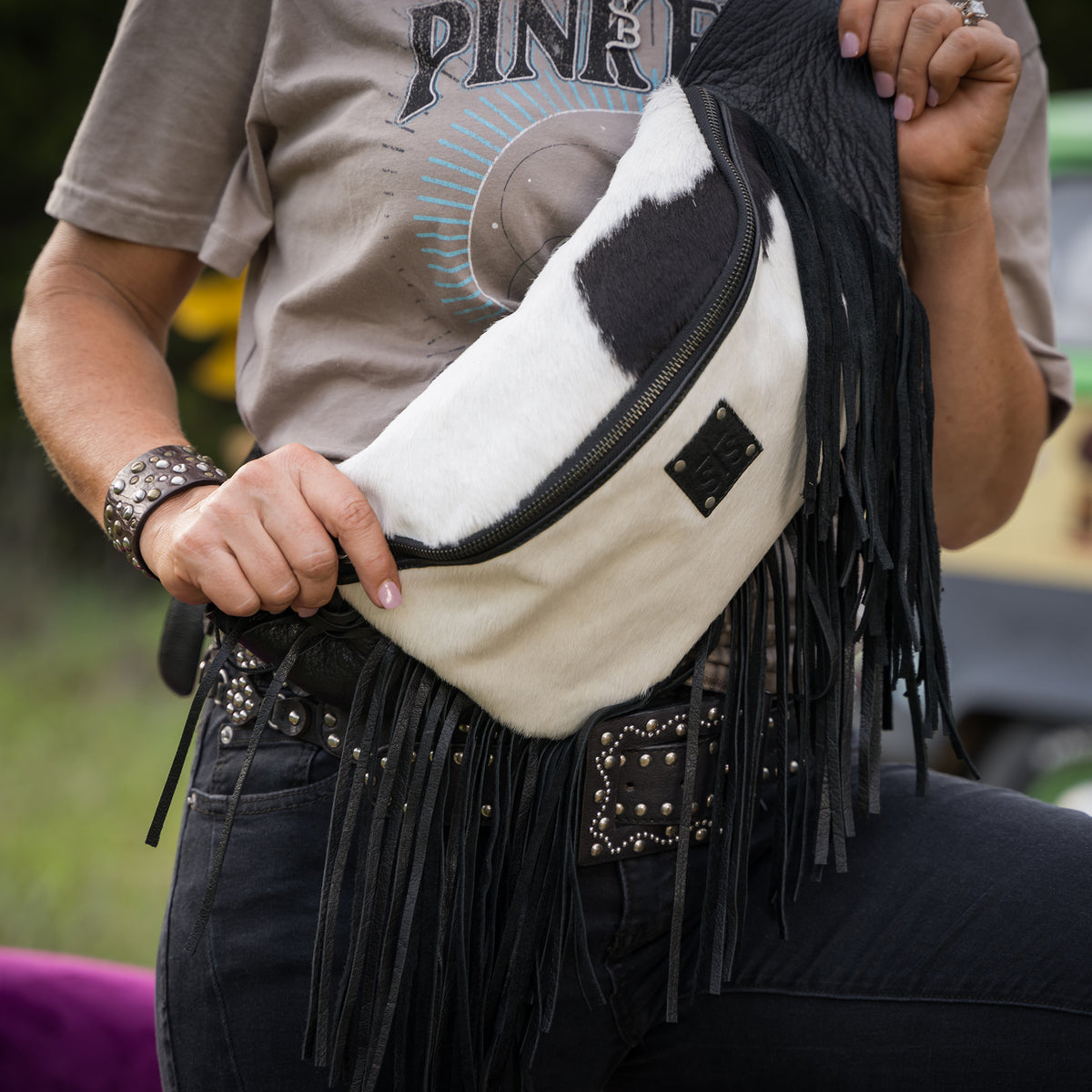 Person holding a white and black fringed bag with studded details.
