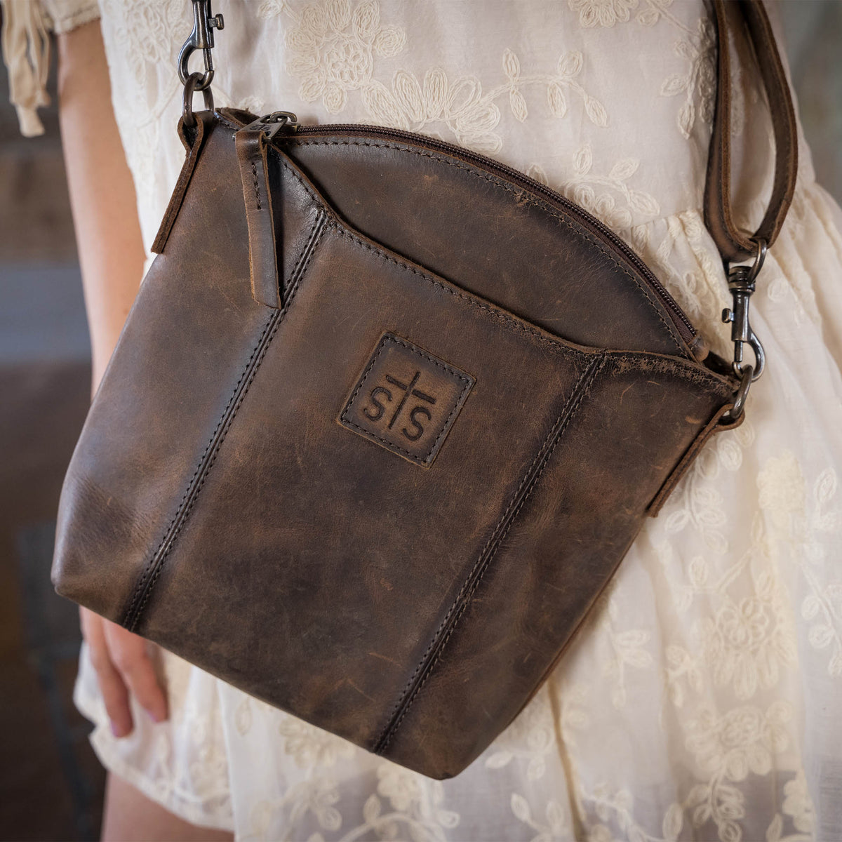 A leather purse with a crossbody strap on a woman's hip.