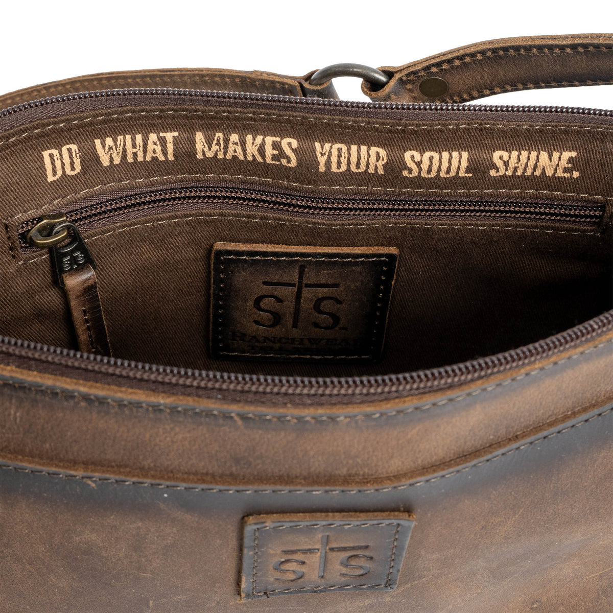 "Do what makes your soul shine." printed in gold letters in the lining of a leather shoulder bag on a white background.