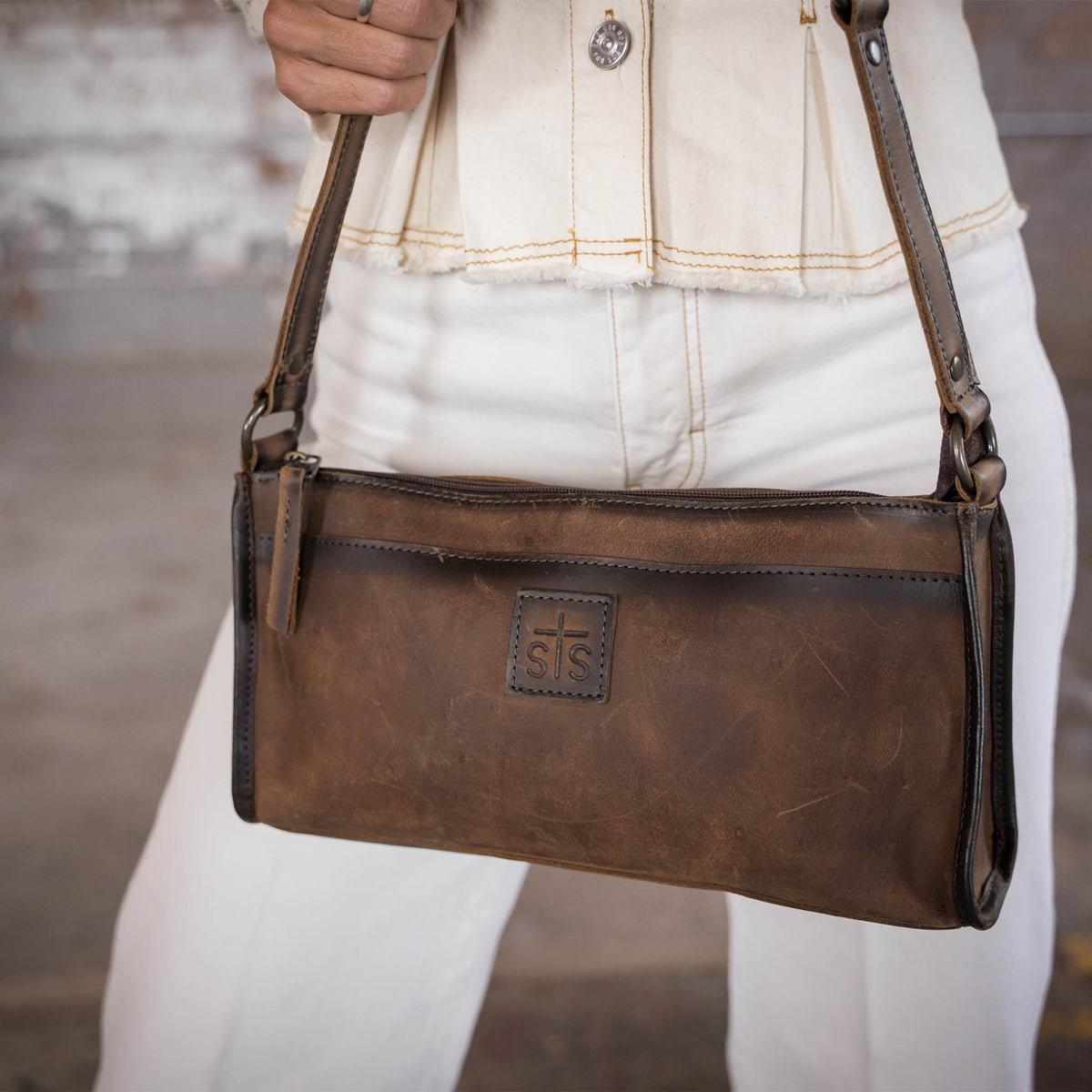 Closeup view of a woman holding a leather shoulder bag with STS patch.