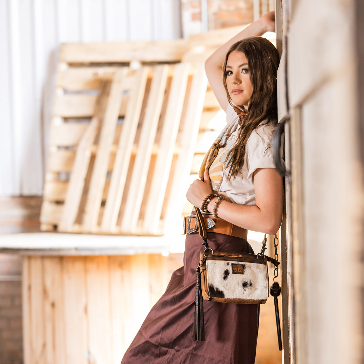 Style Brazile wearing our Cowhide and distressed full grain leather purse with multiple zip closures and adjustable crossbody strap in front of farm doors