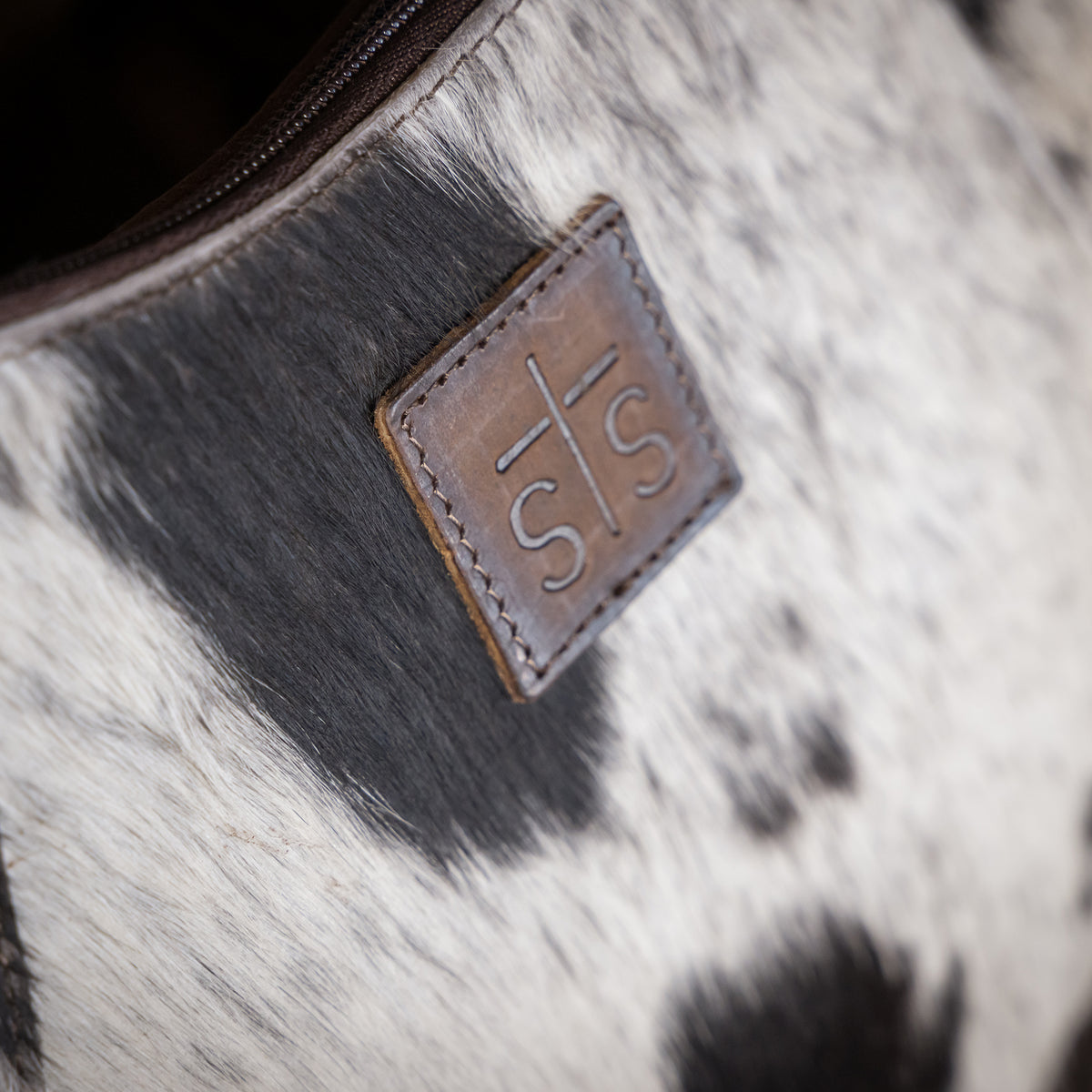 closeup on the STS stamped leather on the front of our leather and cowhide crescent bag with fringe along the bottom 
