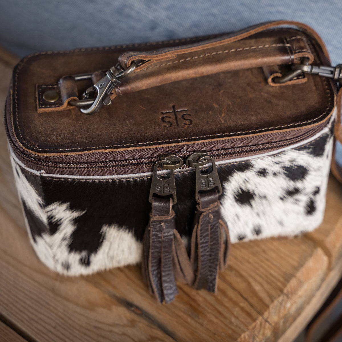top view of our leather and cowhide petite train case with double zip closure with tassels, a top carry handle and adjustable crossbody strap 