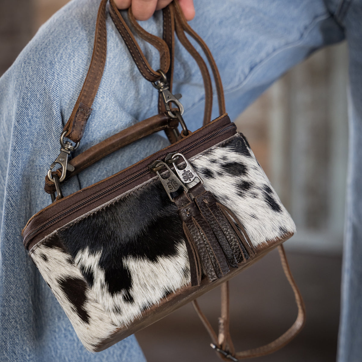 closeup of our leather and cowhide petite train case with double zip closure with tassels, a top carry handle and adjustable crossbody strap 