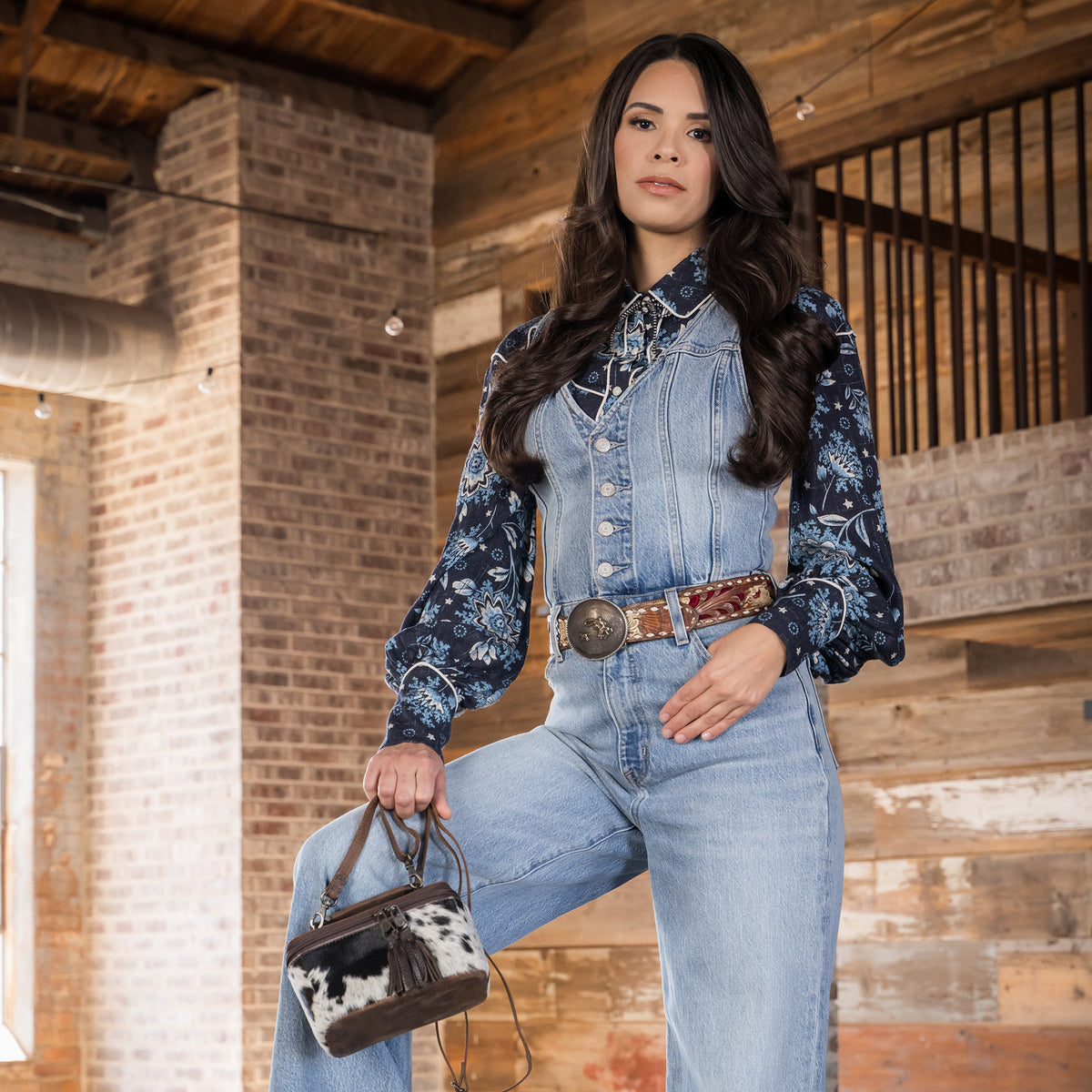 Soni Vest wearing our leather and cowhide petite train case with double zip closure with tassels, a top carry handle and adjustable crossbody strap 