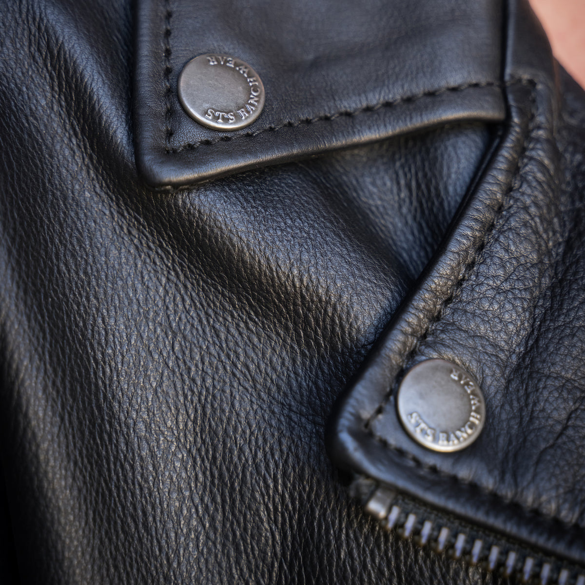 closeup on the collar of our black leather jacket with fringe detailing and asymmetrical zipper front closure 