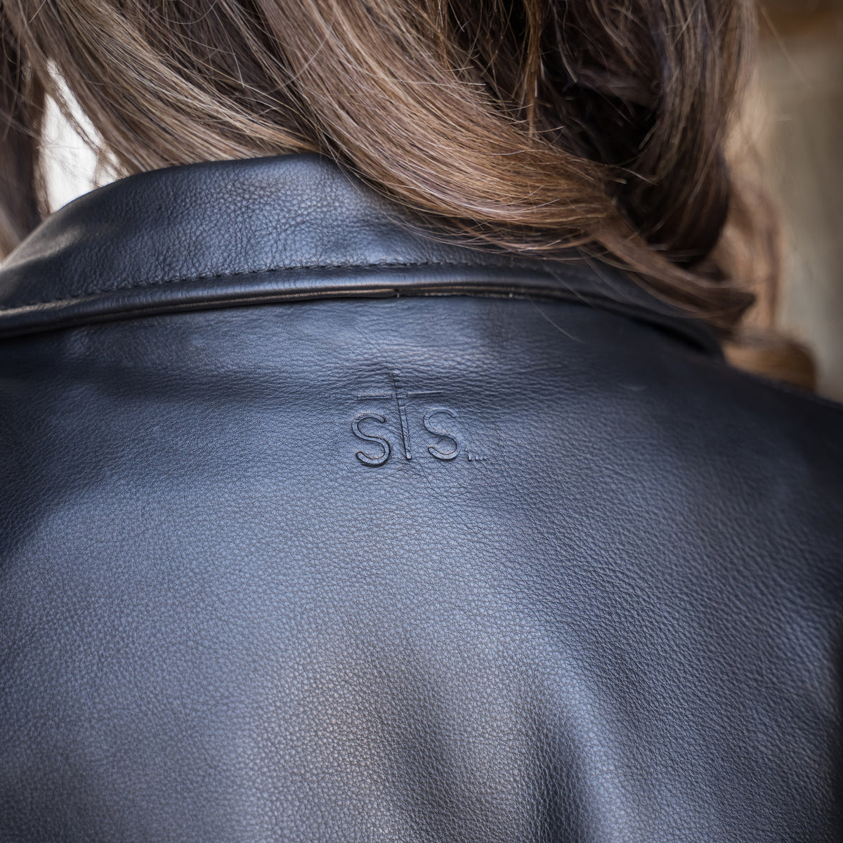 closeup of sts embossed leather on the back of our black leather jacket with fringe detailing and asymmetrical zipper front closure