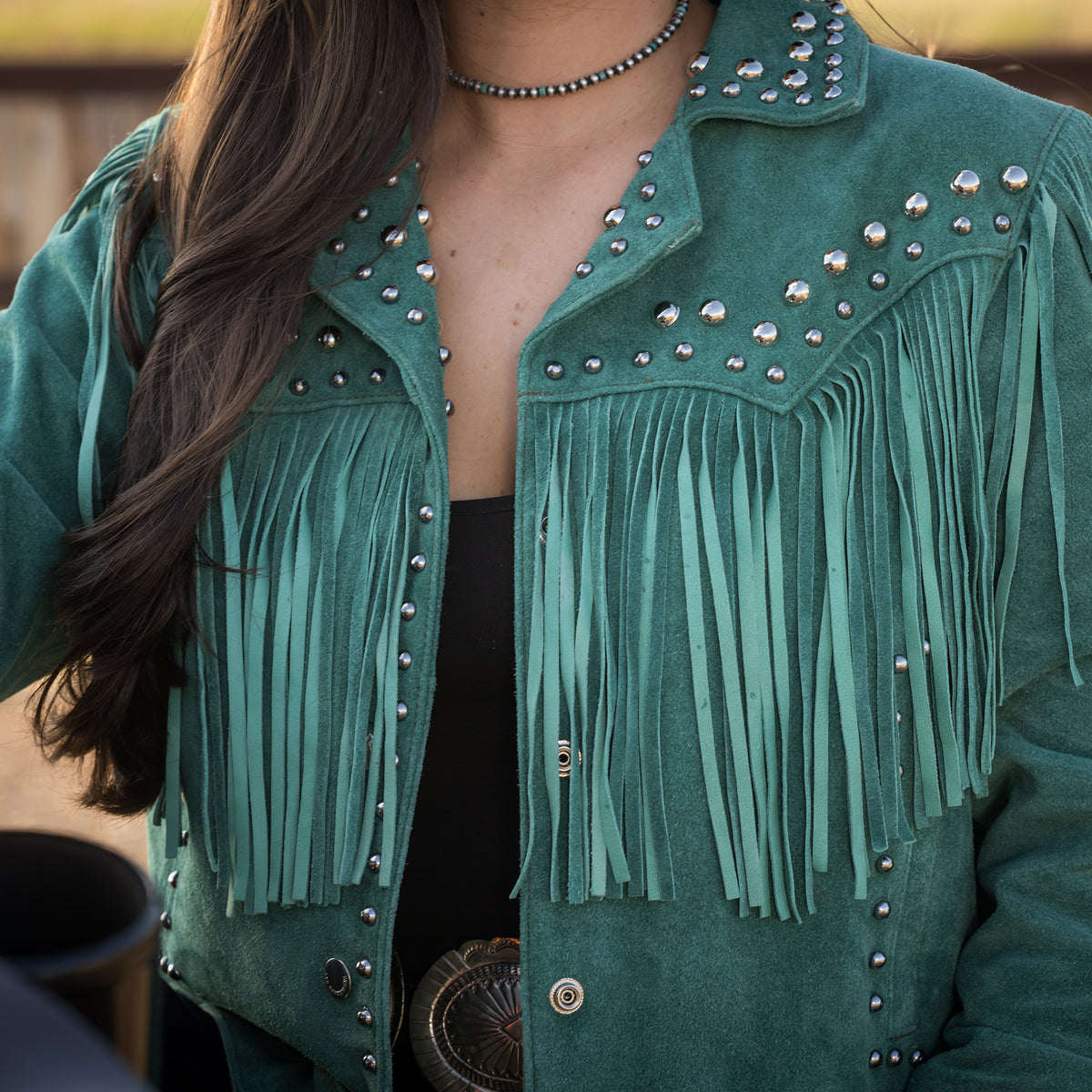 Closeup of the front of our emerald green suede jacket with hand studded detailing, fringe and snap front closure.
