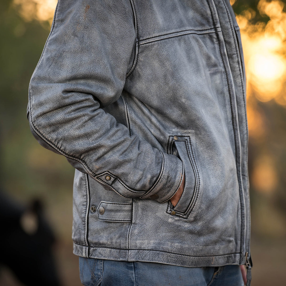 Person standing in the woods with their hands in the jacket pocket of a stonewashed genuine leather Rifleman jacket.