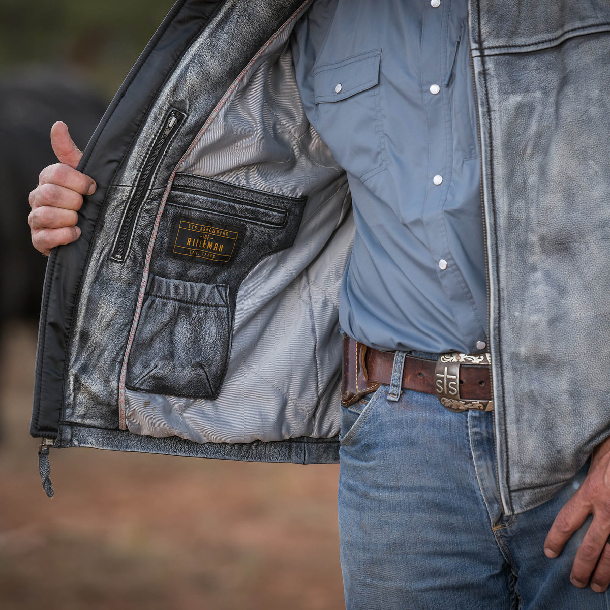 Person holding genuine leather Rifleman jacket open showing inside lining and zip pockets.