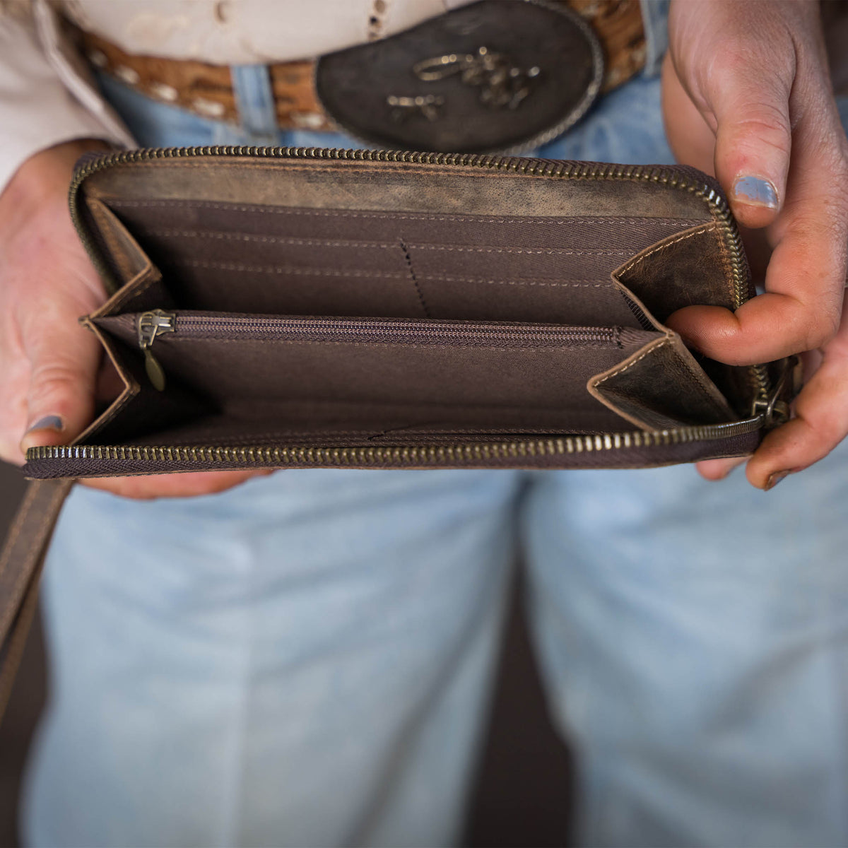 A woman holding open a leather wristlet showing the card slots and coin slot zipper.