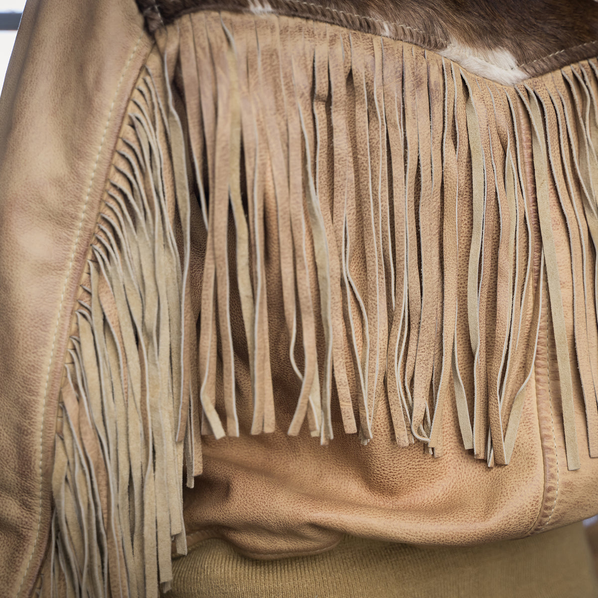 Closeup of the fringe detail on beige leather jacket with cowhide accents.