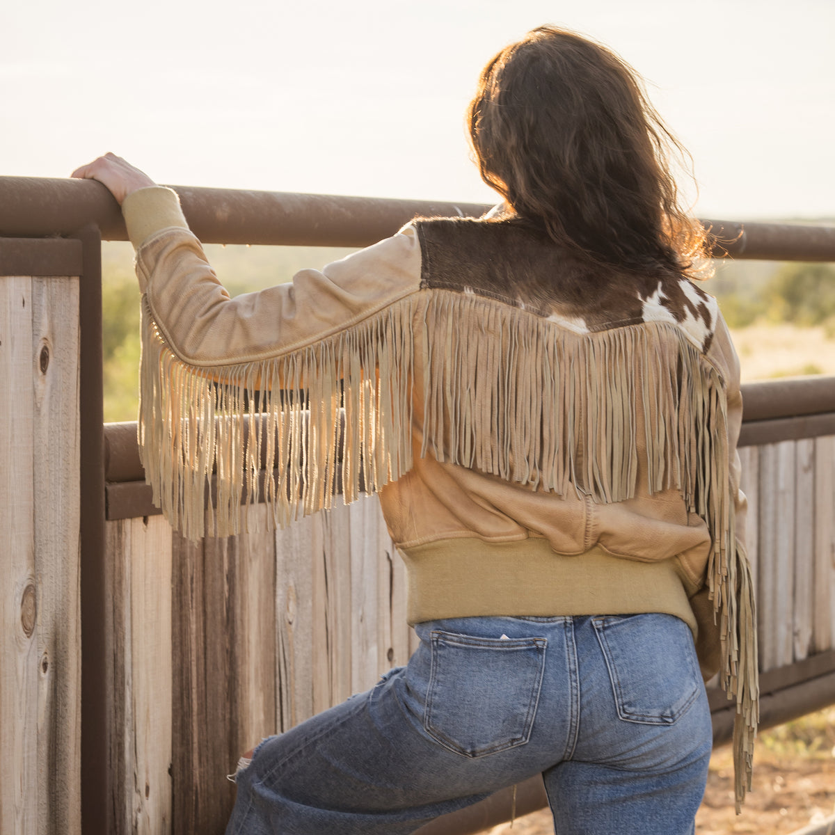 Person facing away wearing a beige leather jacket with cowhide detailing, fringe and western yoke.