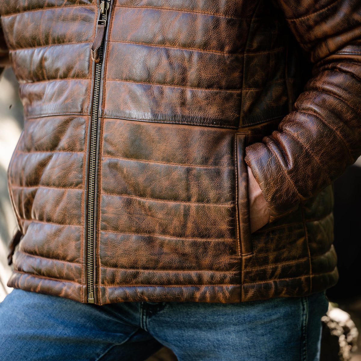 Detail of a brown men's Clyde leather puffer jacket with a full-grain leather exterior, zip front closure, and hand warming pockets.