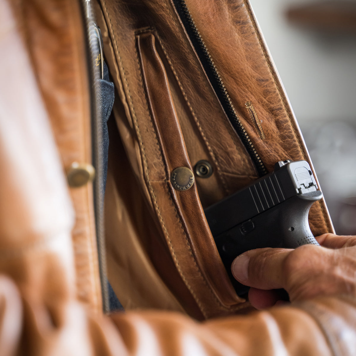 closeup of a weapon in the conceal carry pocket of our brown full grain zip and button front closure with slip hand pockets and chest pockets 